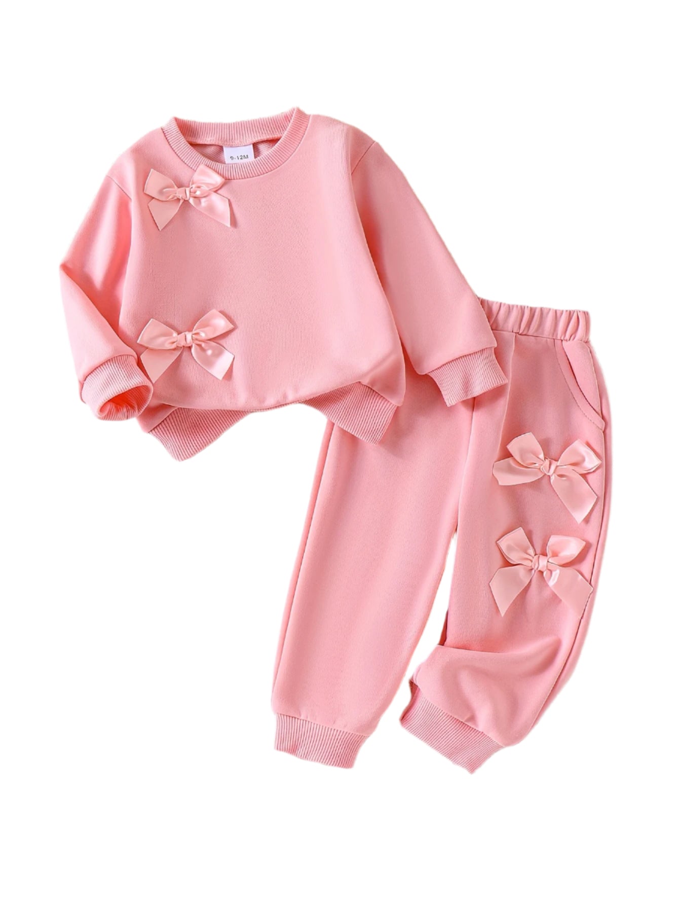 Pink children's outfit with bows on a textured surface with shoes and flowers.