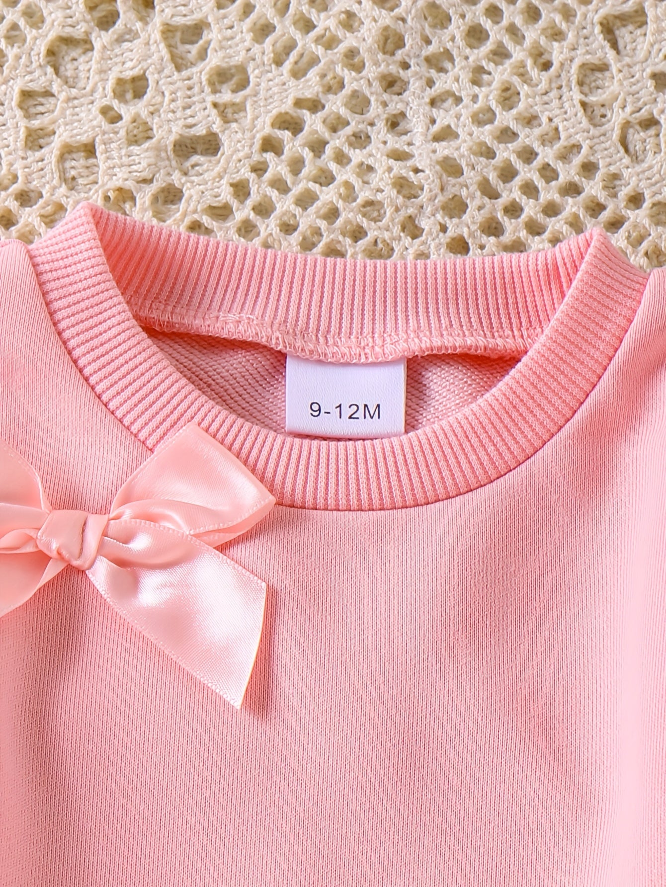 Pink sweater with a bow detail on a textured beige background